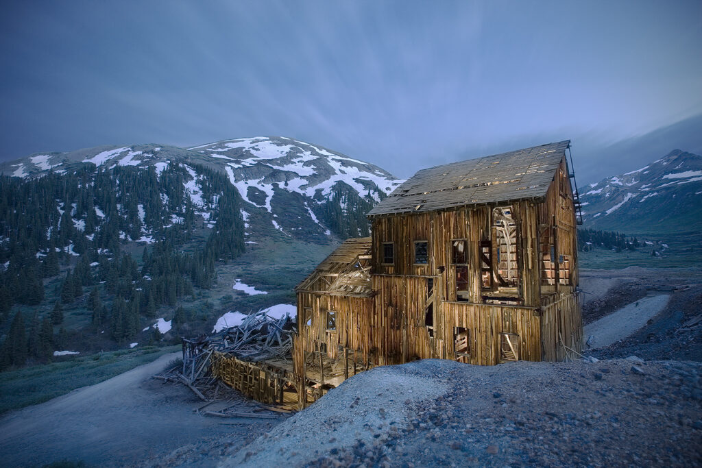 Abandoned wooden house in Animas Forks, Colorado lit at night with star trails and alpine backdrop