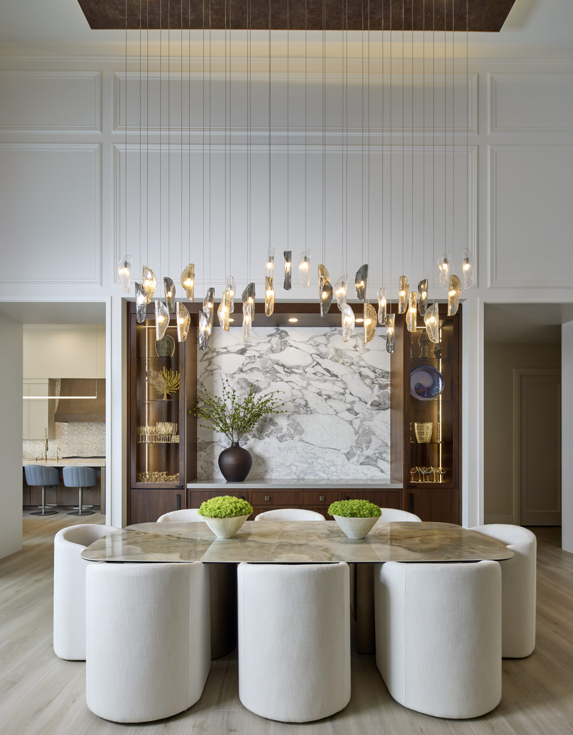Luxury dining room interior design photography in a private Miami residence with sculptural chandelier, marble feature wall, custom wood built-ins, and curved upholstered dining chairs