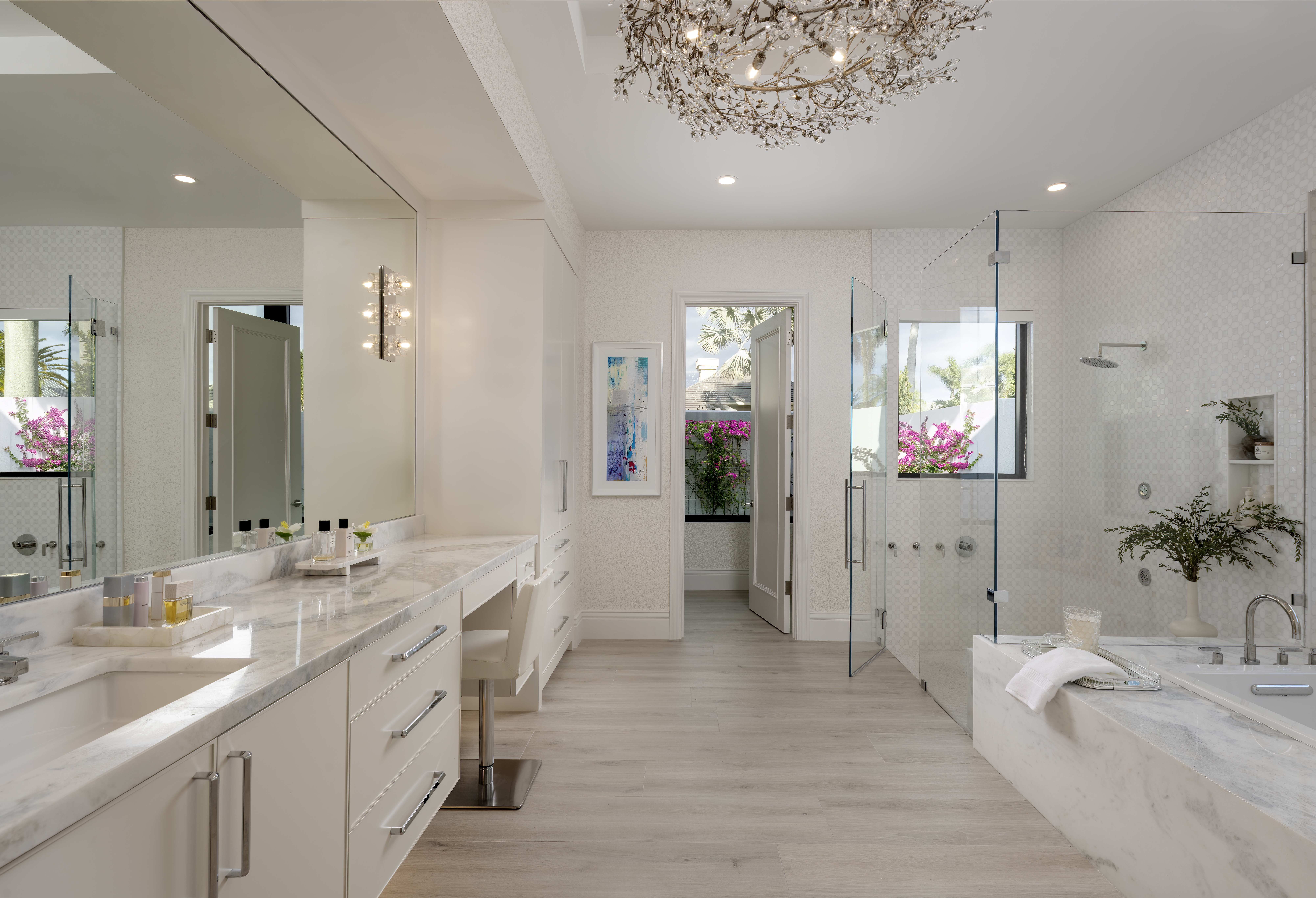 Bright luxury bathroom interior design photography with marble surfaces, glass shower, soaking tub, chandelier, and large vanity in a private residence